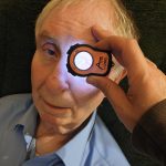 Elderly patient receiving a close-up eye examination at home using the Lumio diagnostic device.