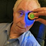 Lumio device emitting blue light during a home fluorescein eye exam on an elderly patient